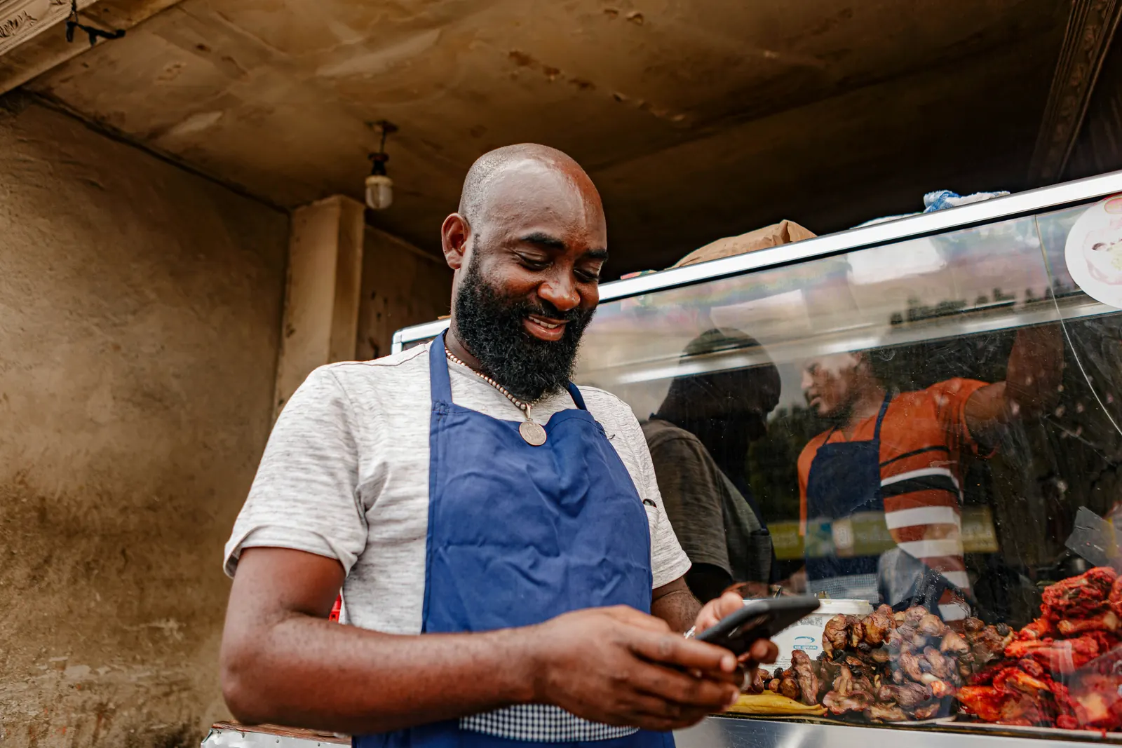 Small business owner smiling while checking his phone at his food stall